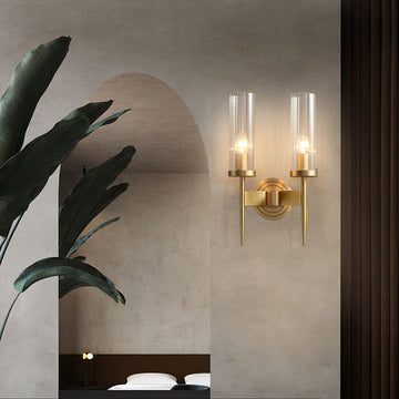A minimalist interior features an American style copper wall lamp with an elegant lighting effect, dual-bulb E14 LED bulbs, and glass covers. A large green plant is placed on the left, complementing a simple bedroom with a curved entryway and nighttime ambiance in the background.