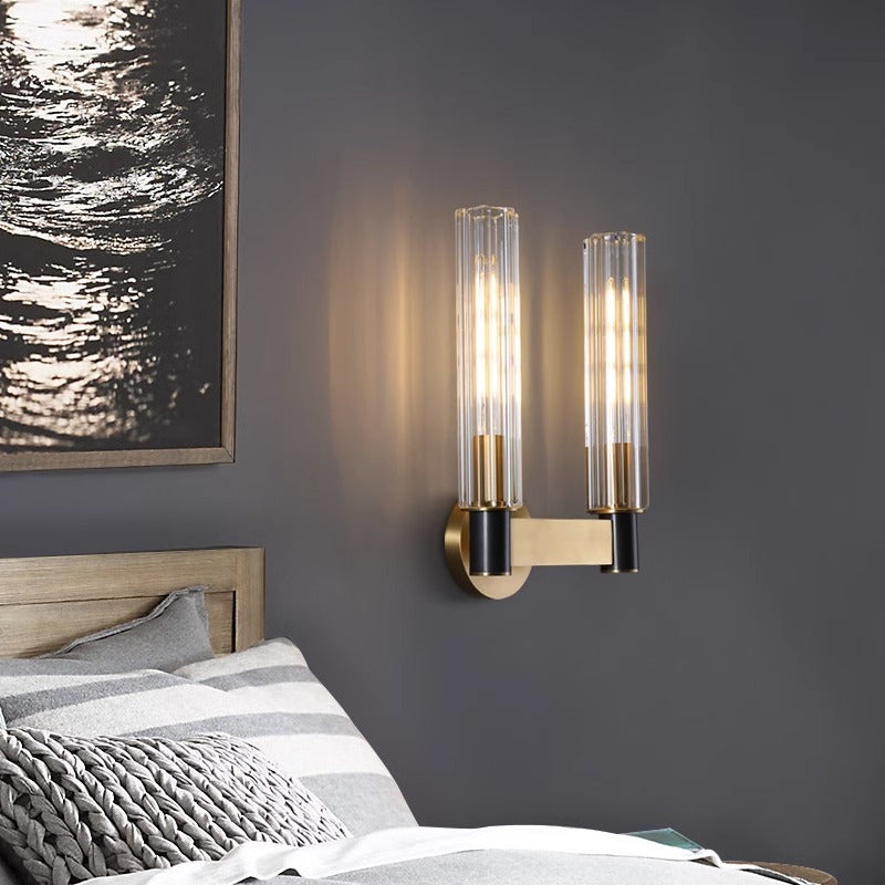 A modern room showcases a minimalist design with two Brass Glass Bedroom Lamps flanking a large gold-framed mirror. Below, an E14 LED warmly illuminates the wooden console table adorned with two ceramic vases and a shallow dish.
