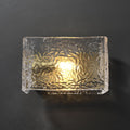 Textured glass wall sconce illuminated on dark background.