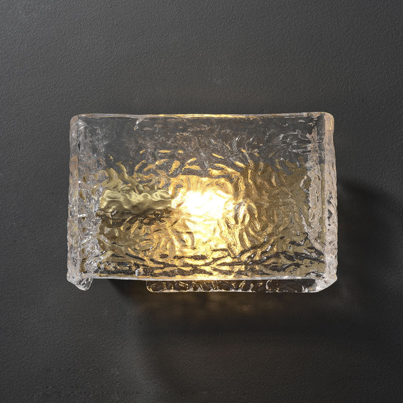 Textured glass wall sconce illuminated on dark background.