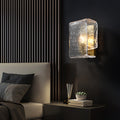 Modern textured wall sconce illuminates beside a bed with gray bedding and small bedside decor.