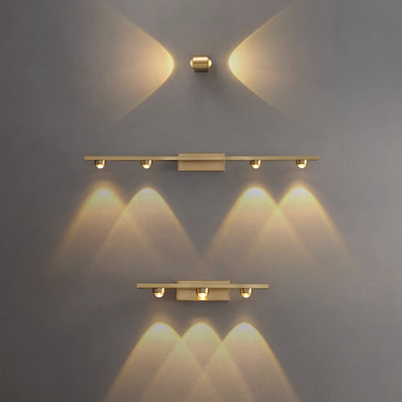 The Linear brass wall light, featuring Osram Chip technology, offers a minimalist design with warm yellow lights and three horizontal fixtures, casting soft patterns on a gray wall. Its sleek modern aesthetic and 3500K color temperature blend style and functionality harmoniously.