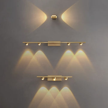The Linear brass wall light, featuring Osram Chip technology, offers a minimalist design with warm yellow lights and three horizontal fixtures, casting soft patterns on a gray wall. Its sleek modern aesthetic and 3500K color temperature blend style and functionality harmoniously.