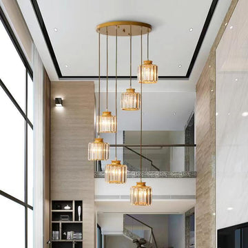A modern interior features a two-story ceiling highlighted by the breathtaking Waterfall Stair Chandelier. This gold-toned fixture with six glass pendant lights crowns the space, complemented by large windows and neutral colors for a serene, modern decor.