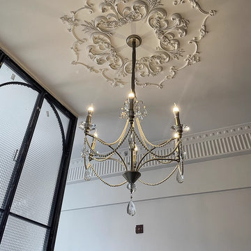 An ornate chandelier hangs gracefully in a room, complementing a beautifully designed staircase that adds to the ambiance.