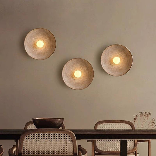 Three Japanese Retro Wall Lamps with LED G4 bulbs illuminate a beige wall. Below, a dark wood dining table is paired with chairs featuring rattan backs. A decorative bowl and dried flowers complete the minimalist Wabi-Sabi ambiance.