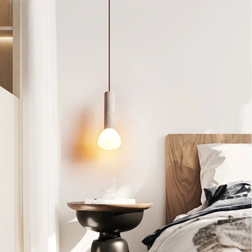 A minimalist bedroom is lit by a Nordic Stone Chandelier, enhancing the serene atmosphere. Below it sits a small black round side table with a glass of water, while the bed features a wooden headboard and white bedding, beautifully illuminated by the chandeliers glow.