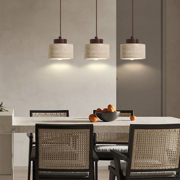A dining room with a rectangular table, four woven chairs, and a bowl of oranges sits under three Nordic Style Restaurant Chandeliers casting a warm glow. The decor features neutral tones, simple lines, and natural yellow limestone accents.