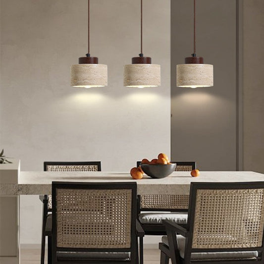 A dining room with a rectangular table, four woven chairs, and a bowl of oranges sits under three Nordic Style Restaurant Chandeliers casting a warm glow. The decor features neutral tones, simple lines, and natural yellow limestone accents.