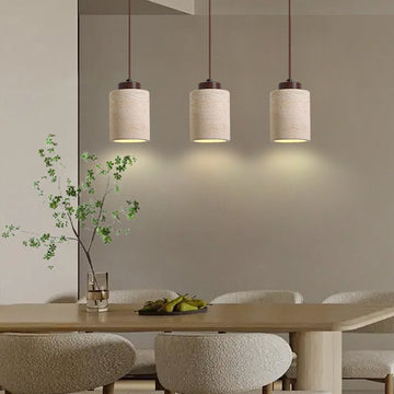 A modern dining area includes a wooden table with four upholstered chairs. Above the table, three Nordic Style Restaurant Chandeliers hang in a row, each featuring LED bulbs. A decorative branch with small green leaves and a fruit tray adorn the table.