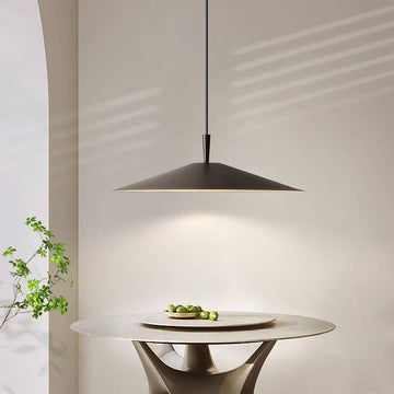 A modern dining space showcases a minimalist round table under the sleek black UFO Restaurant Chandelier. The ambient vibe is enriched by its adjustable height and smart dimming, with green apples on a plate. A small green-leafed plant graces the left side against a light-toned wall.