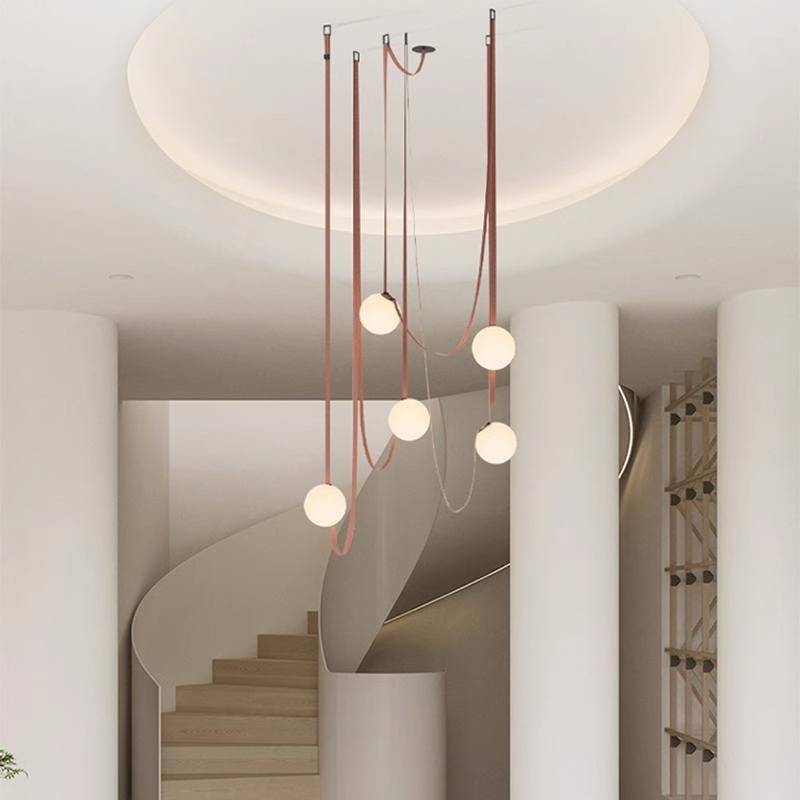The modern living room showcases a large white textured wall and an elegant Branch Chandelier offering customizable dimming options. Plush, muted-tone seating encircles a round black coffee table next to a small tree, creating minimalist decor that emphasizes energy-efficient lighting.