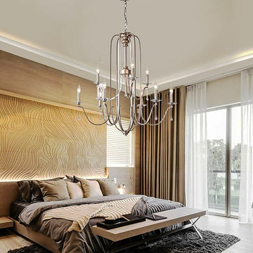 A modern bedroom features a large, stylish bed with pillows and a blanket, a textured wave design on the wall behind, and sheer curtains over floor-to-ceiling windows. The Mid Century Vintage Candle Chandelier glistens overhead, completing the elegant look.