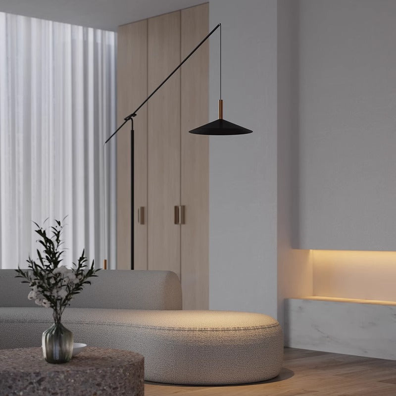 Minimalist living room with a modern, curved beige sofa. A tall, angled black floor lamp stands beside it. Soft lighting from a recessed shelf illuminates the wall, with sheer curtains adding elegance.