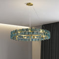 The Chandelier Series offers a modern lighting solution with adjustable height, featuring two golden concentric rings with blue glass panels. It creates a warm ambiance in a room with gray curtains and beige walls, embodying sleek design.