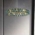 The Chandelier Series features a modern glass pendant light with a circular design, a gold frame, and blue-tinted geometric glass. It offers elegance against a neutral gray wall, and its adjustable height ensures versatility in any space.