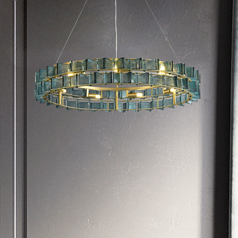 The Chandelier Series features a modern glass pendant light with a circular design, a gold frame, and blue-tinted geometric glass. It offers elegance against a neutral gray wall, and its adjustable height ensures versatility in any space.