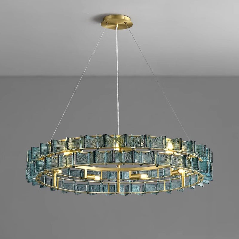 The Chandelier Series features a modern circular design with a gold frame and layered transparent blue glass rectangles. This elegant pendant light is suspended by three cords from a gold ceiling mount on a gray background, offering adjustable height for versatile installation.