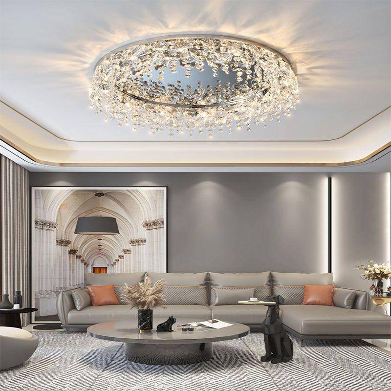 An elegant living room boasts a Butterfly Crystal Ceiling Lamp with LED bulbs, casting a soft glow over a gray sofa accented by orange cushions. A circular coffee table and archway wall art add charm, while plants and a statue enhance the ambiance in soft, neutral tones.