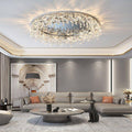 An elegant living room boasts a Butterfly Crystal Ceiling Lamp with LED bulbs, casting a soft glow over a gray sofa accented by orange cushions. A circular coffee table and archway wall art add charm, while plants and a statue enhance the ambiance in soft, neutral tones.