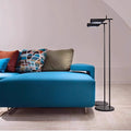 A modern living room includes a bright blue sofa adorned with colorful geometric-patterned cushions, complemented by a Simple floor lamp with a minimalist design standing on a light wooden floor. The walls, in an off-white shade, enhance the rooms tranquil ambiance.