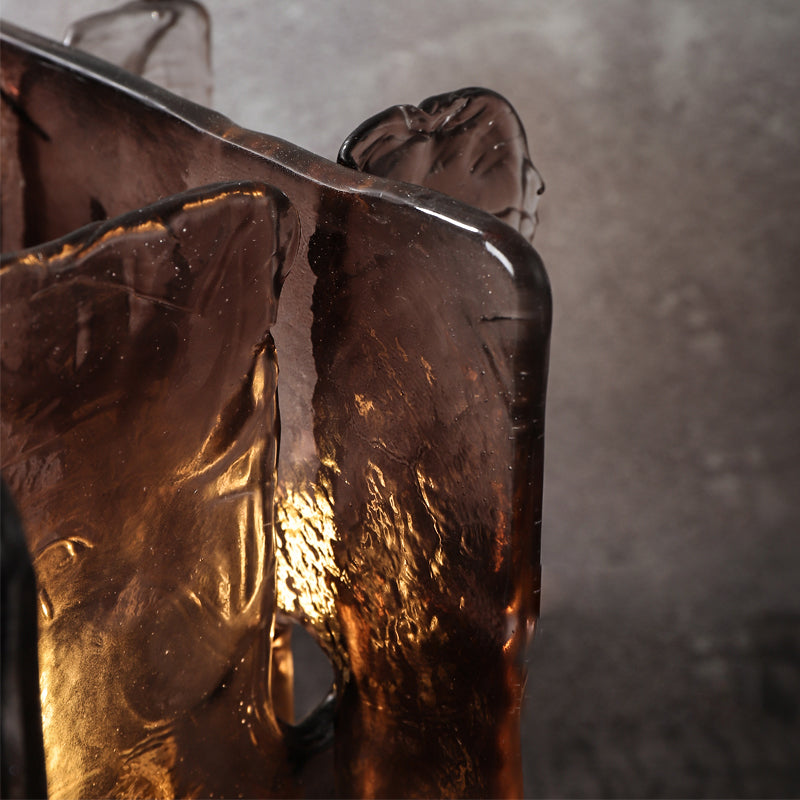 A close-up of hand-blown amber glass shade with a translucent, textured surface illuminated by warm light from behind showcases its uneven, sculptural form. This glowing effect resembles an elegant Vintage brass glass table lamp set against a muted gray background.