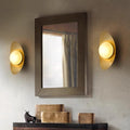 A rectangular mirror with a dark frame hangs on a light wall, flanked by Metal Boat-Shaped Wall Lights. Below, a dark shelf holds small decor items like a sculpture and books, enhancing the spaces modern-style lighting and chic elegance.