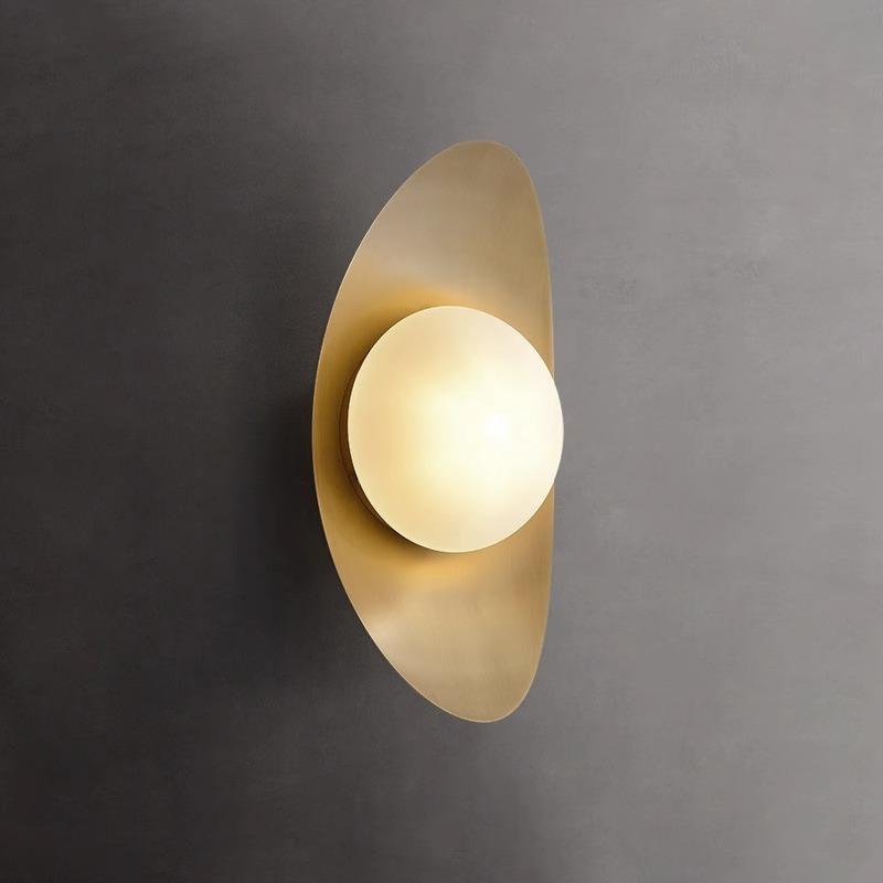 The Metal Boat-Shaped Wall Light showcases chic elegance with an orb-shaped bulb on a golden elliptical plate, embodying minimalist design against a smooth gray wall.