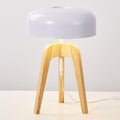 The Tripod Floor Lamp features a sleek, minimalist design with a white dome-shaped shade and a natural wooden tripod base. It sits on a white surface, with its white cord extending below.