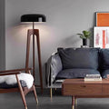 Modern living room featuring a sleek Tripod Floor Lamp, a plush-cushioned dark gray sofa, and a wooden coffee table. A mid-century chair draped with a white fur throw sits beside the sofa, while a potted plant and framed artwork enhance the decor.
