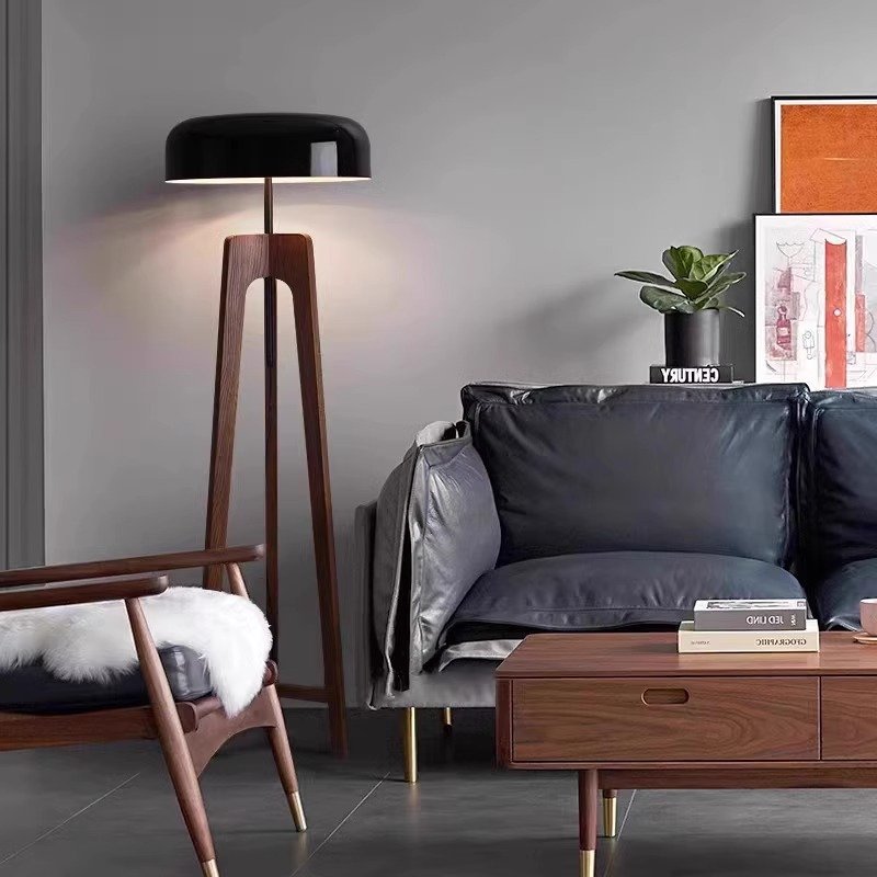 Modern living room featuring a sleek Tripod Floor Lamp, a plush-cushioned dark gray sofa, and a wooden coffee table. A mid-century chair draped with a white fur throw sits beside the sofa, while a potted plant and framed artwork enhance the decor.
