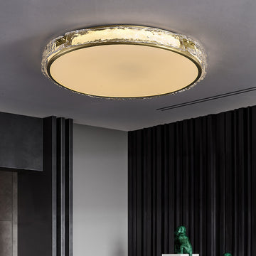 Modern golden ceiling light fixture in a room with dark curtains and part of a green statue visible.