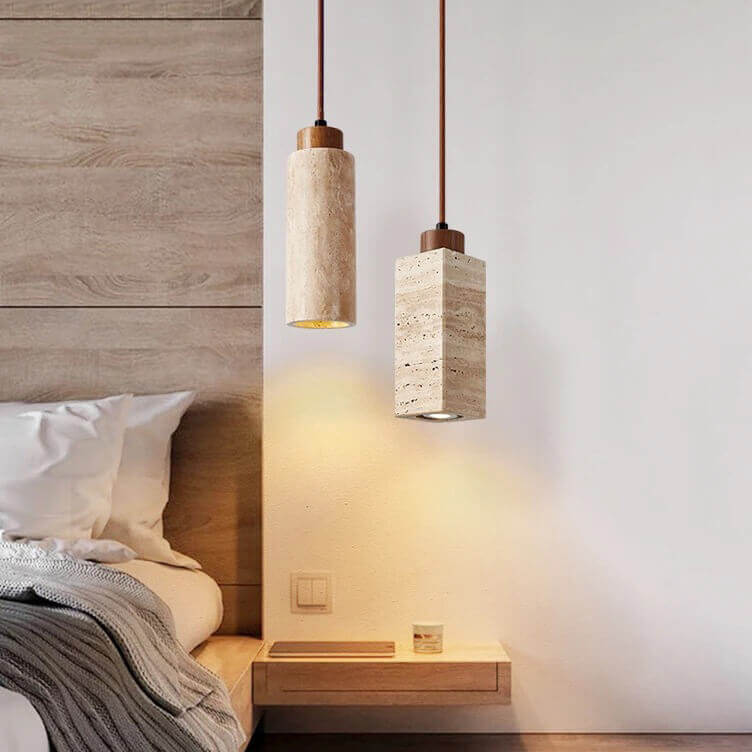 A cozy bedroom corner showcases a Travertine Restaurant Chandelier with dimmable LED bulbs above a wooden bedside table. A neatly made bed with white linens and a gray blanket complements the wooden panel wall, enhancing the modern minimalist decor.
