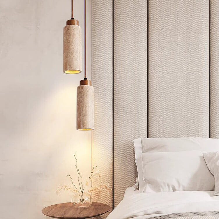 In a stylish bedroom, a bed with white pillows and sheets rests against a textured beige wall. Above the wooden side table, two Travertine Restaurant Chandeliers hang, fitting perfectly in modern minimalist interiors, featuring dimmable LED bulbs beside a vase of dried plants.