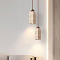 Two rectangular pendant lights, inspired by the Travertine Restaurant Chandelier, illuminate a minimalist light gray wall. Below, a gray sofa corner and the edge of a wooden surface enhance the modern minimalist interior.