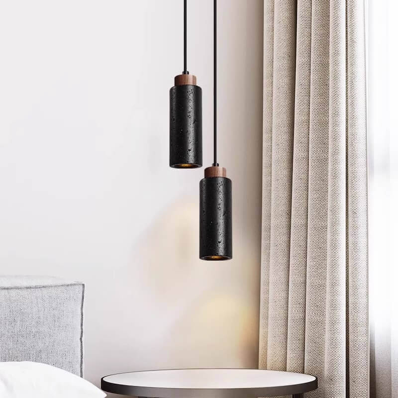 A minimalist bedroom showcases two cylindrical black pendant lights with dimmable LED bulbs above a small round side table. A gray pillow on the bed and a long beige curtain add elegance, reminiscent of the Travertine Restaurant Chandelier.