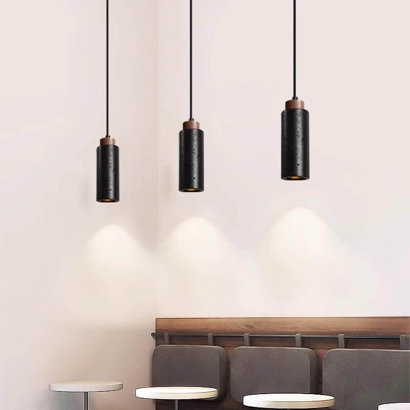 Three black pendant lights with dimmable LEDs hang over a wooden bench, paired with round white tables. The soft glow illuminates a light beige wall, creating a modern, minimalist ambiance reminiscent of the elegance in the Travertine Restaurant Chandelier.