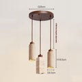 The Travertine Restaurant Chandelier boasts a round, brown base with three cylindrical lights in stone-textured casings. Ideal for Nordic interiors, it features D25cm base, H18.5cm each light, and D6.5cm cylinders, with an adjustable line up to 170cm.
