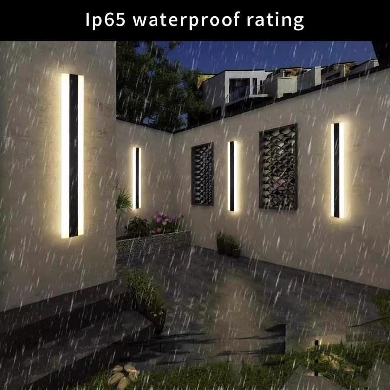 Outdoor Linear Wall Lights with IP65 waterproof rating illuminate a modern courtyard at night during rain. Sleek, vertical fixtures adorn each wall, and plants in planters are visible.