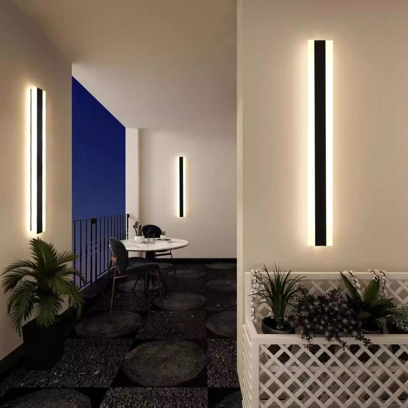 At dusk, an outdoor balcony features IP65 waterproof Outdoor Linear Wall Lights emitting a soft glow. A small round table with chairs and potted plants line the railing, while a planter box of flowers adds charm to the floor.