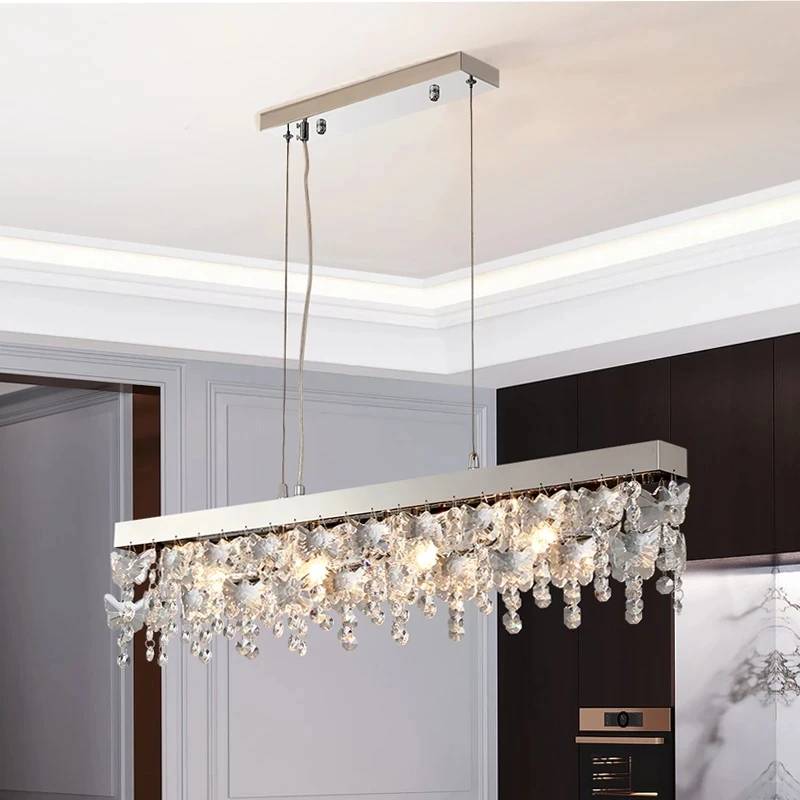 The Crystal Butterfly Chandelier boasts a modern rectangular design with cascading K9 crystals, offering an elegant touch to contemporary spaces. It emits a warm glow while suspended by two thin wires from its adjustable base.