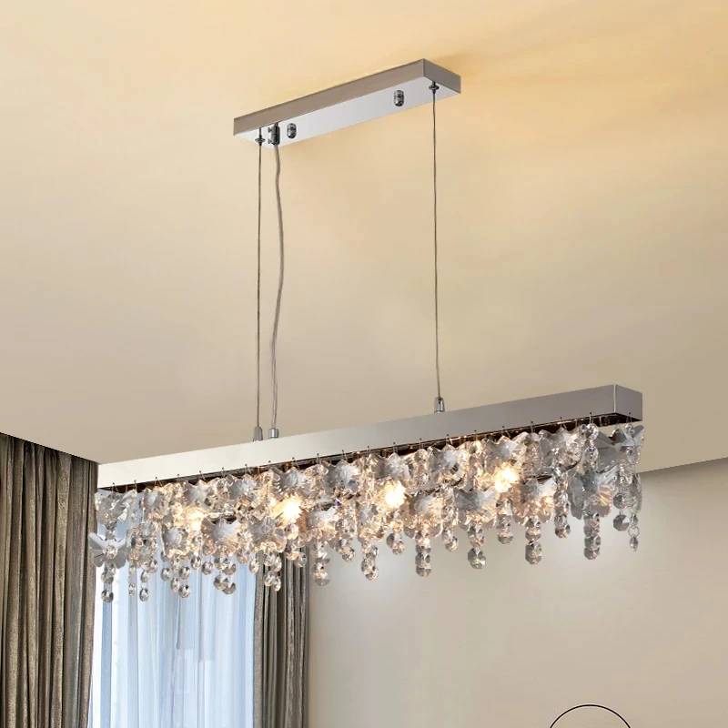 A modern Crystal Butterfly Chandelier graces the ceiling, adorned with K9 crystals and multiple lit bulbs, casting a warm glow. The beige ceiling complements its shimmering elegance while gray curtains are partially visible in the background.
