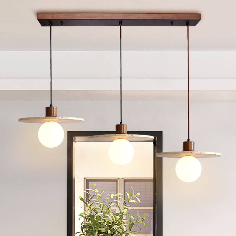 The Vintage Yellow Travertine Chandelier, featuring three glowing bulbs each encircled by flat circular shades evoking vintage elegance, hangs gracefully from the ceiling. Below it, a potted plant adds a touch of natural charm in the foreground.