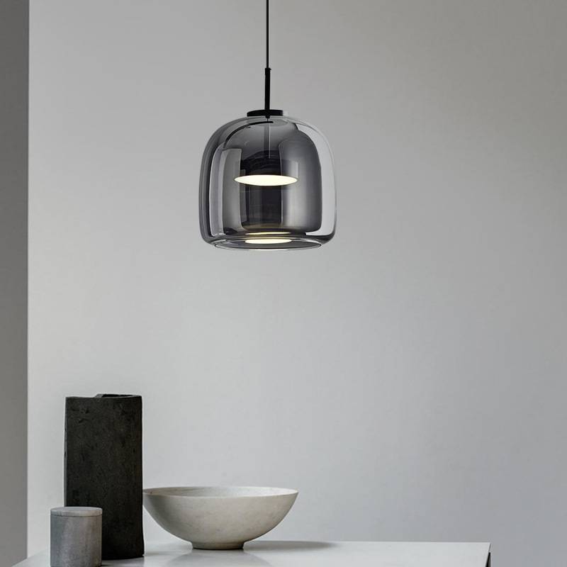 A modern interior features a sleek, Retro Chandelier with an adjustable hanging wire, casting a warm white glow over a round white bowl and tall cylindrical stone object on a white table against a light gray wall.