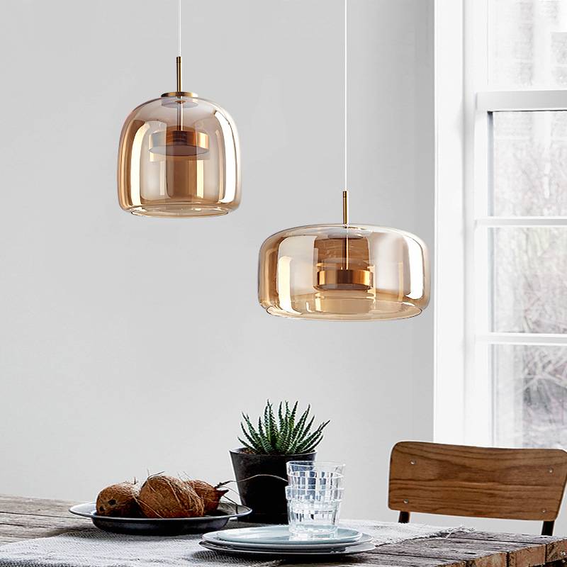 A stylish kitchen features a Retro Chandelier with an adjustable hanging wire, casting warm white light. A wooden dining table is adorned with a potted succulent, coconuts, plates, and glasses. A wooden chair and large window complete the bright, modern space.