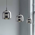 Three Retro Chandelier lights with glossy glass shades in different sizes hang from adjustable wires, aligned in a row against a light gray wall by a large window streaming natural light.