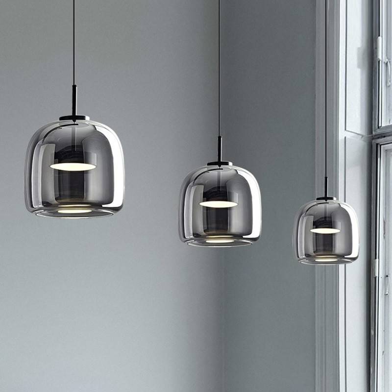 Three Retro Chandelier lights with glossy glass shades in different sizes hang from adjustable wires, aligned in a row against a light gray wall by a large window streaming natural light.