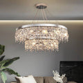 The Crystal Butterfly Chandelier, adorned with cascading K9 crystals, casts a warm glow above a modern grey couch. White cushions and green plants enhance the elegance of the space, while its adjustable lighting adds both style and function.