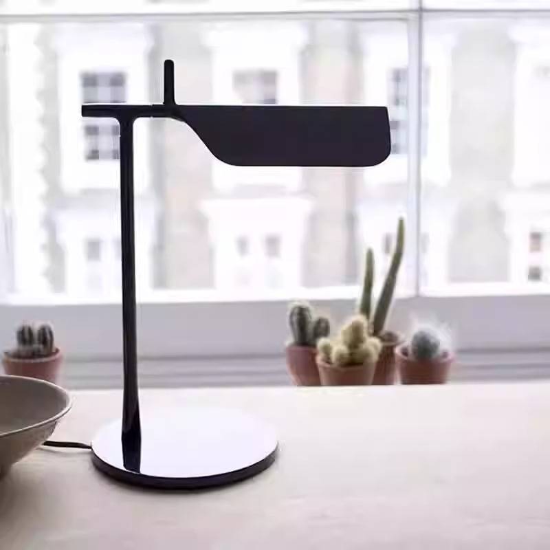 The Simple Desktop Lamp, boasting a sleek black design with LED lighting, sits by a large window lined with small potted cacti. A blurred cityscape forms the backdrop, capturing minimalist elegance.