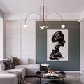 A modern living room showcases a gray sectional, a minimalist black coffee table, and a large abstract painting of a black brushstroke silhouette on a green accent wall, all highlighted by the contemporary St Kilda Chandelier with red globe lights hanging from the ceiling.